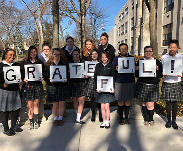 Students holding signs that spell out Grateful. Links to Gifts by Estate Note